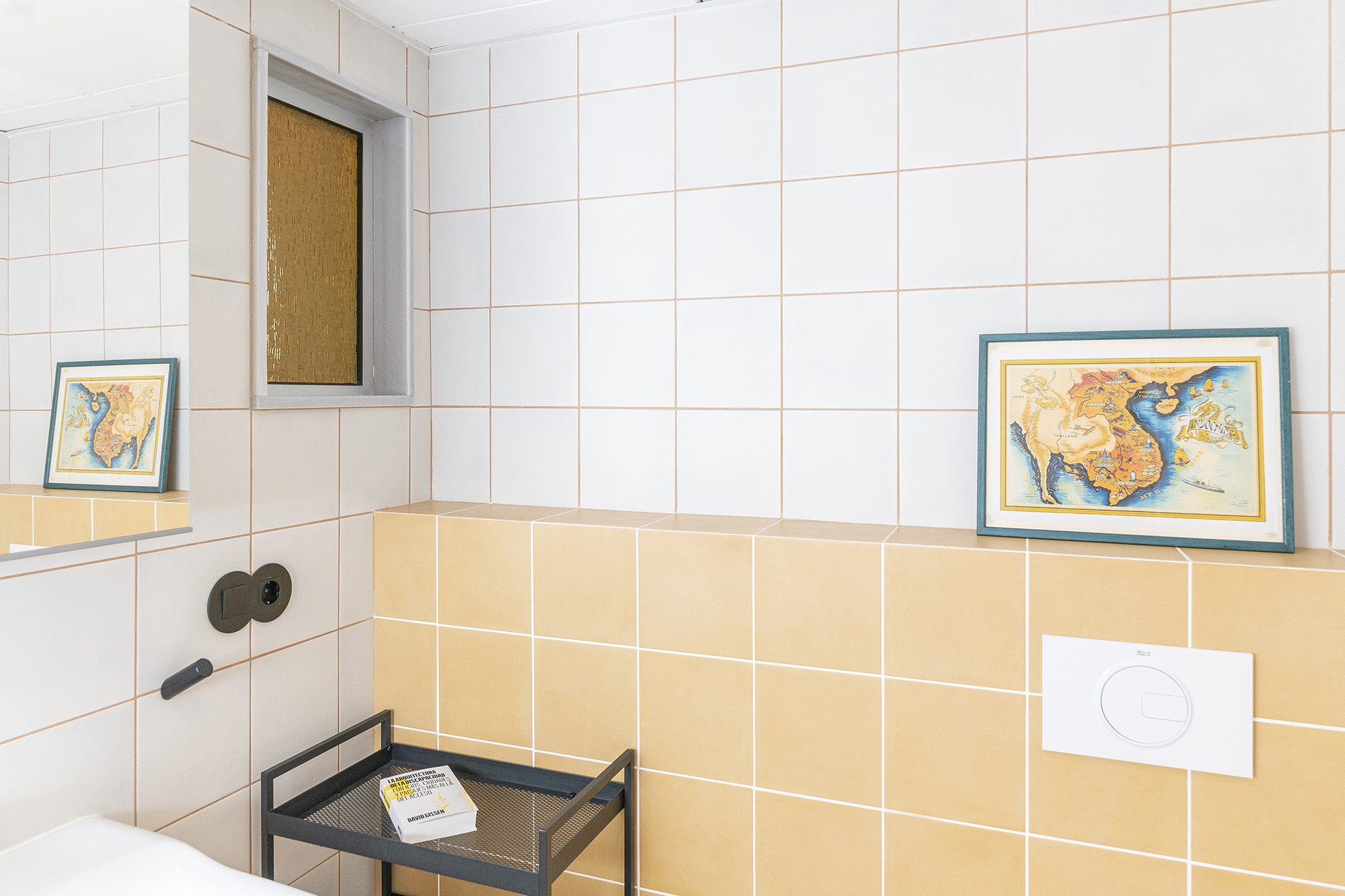 Ventana interior con vidrio recuperado de color amarillo que pasa la luz entre los dos baños.